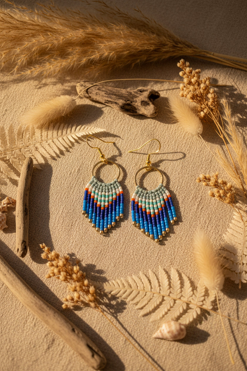 Boucles d'oreilles Cheyenne Courte tons marins posées sur fond naturel avec herbes séchées et coquillage – ambiance bohème estivale
